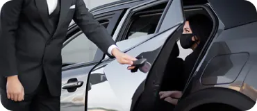 A chauffeur opening the door of a black car for a passenger.