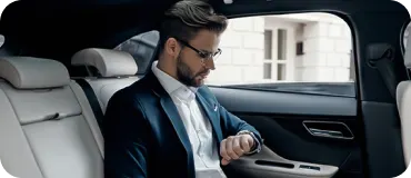 A businessman sitting inside a luxury car interior and checking his watch.