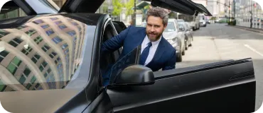 A smiling man in a blue suit stepping into a black luxury car.