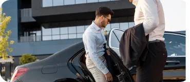 A casually dressed man loading luggage into the back of a luxury car.